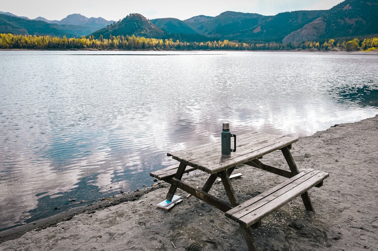 services-02 Serene lakeside scene with a picnic table beside calm water under a clear autumn sky.