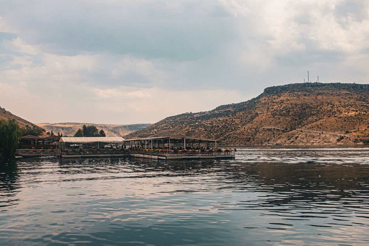 hero-img-01 A serene lakeside view featuring a floating restaurant against desert hills and cloudy sky.
